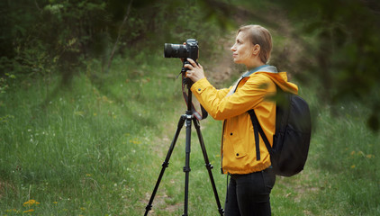 Side view of woman standing in green forest using tripod taking nature pictures, half body portrait