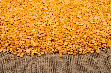 Yellow split peas scattered on a background of coarse-textured burlap. Traditional cereals for making soups and porridge. Close up.