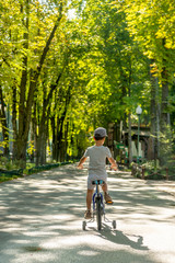 Child rides bike on road in park, rear view