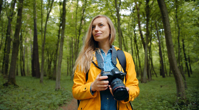 Woman holding digital camera walking through green leafy forest admiring spring or summer nature