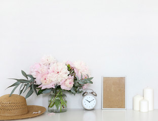 Peonies in the interior on the table, clock alarm clock, craft boxes, candles