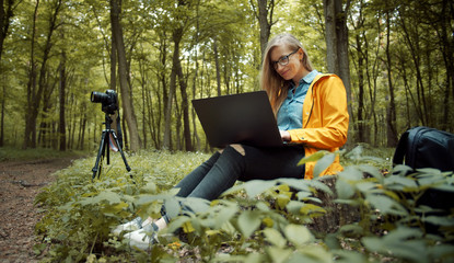 Professional photographer sitting on stump in spring woods using laptop to check what she has taken