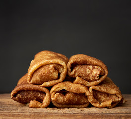 twisted thin fried pancakes with filling lie in a stack on a wooden board