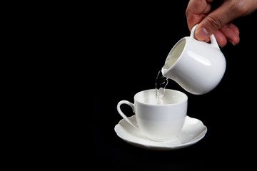 Hands adding sugar to tea cup on black background. Close up of woman's hands adding glucose syrup in coffee cup or tea for Consume less sugar. Reduce sugar consumption concept