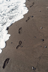 Sandy beach by the ocean. The wave washes away the footprints of a person. Travel and vacation.