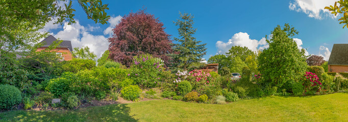 Panoramic view of a beautiful landscape garden with green lawn and a colorful flower bed. Summer...
