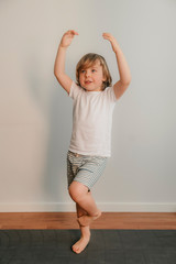 Smiling boy practicing yoga, standing in Vrksasana exercise with namaste, tree pose, working out with sportswear, t-shirt, pants, full interior