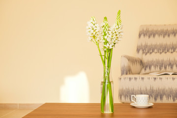 Empty apartment with minimalistic style interior, coffee table with bouquet in glass vase on foreground. Copy space for text, background, close up.