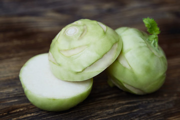 Two raw kohlrabies on the rustic wooden table, one of which is cut in half.