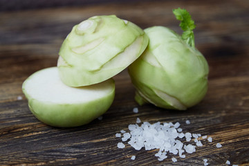 Two raw kohlrabies on the rustic wooden table with a pinch of coarse sea salt. One kohlrabi is cut in half.