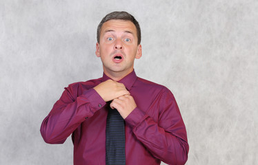 Frightened man in a red shirt is tying a blue tie.