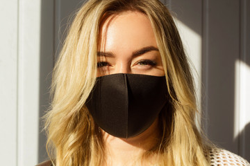 Picture of young blond woman wearing black protection mask at daylight