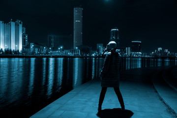 unrecognizable person in against backdrop of skyscrapers of the night city. She is wearing a gas mask. fear of contagion. global pandemic. biohazard and health concept.