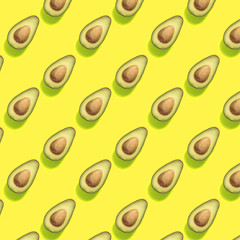 Pattern with half of avocados on trendy yellow color background. Food pattern.