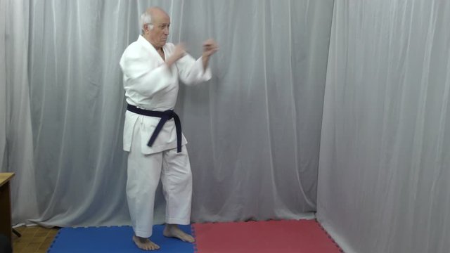On a red and blue tatami, an old male athlete is training kicks and kicks