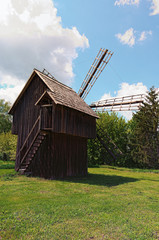 Fototapeta na wymiar Pereyaslav, Ukraine-May 16, 2020: Picturesque view of ancient wooden wind mill in spring sunny day. Beautiful old trees in the background. Blue sky background with white clouds