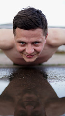 Young man doing pushups over a puddle after rain on a playground