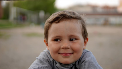 Portrait of little cute boy in grey jacket in playground.
