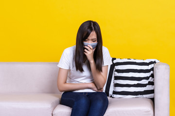 Obraz premium Asian woman sitting on sofa wearing protective face masks coughing or sneezing. Sick woman with flu wearing mask,feeling sick, coughing, wearing mask protection against flu. New coronavirus 2019.