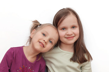 Two little sibling little girls hugging each other and smiling on light background