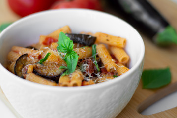Traditional Italian dish: pasta alla norma with tomatoes, eggplant, garlic, basil and ricotta cheese on a wooden cutting board