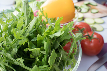 arugula in a plate on the kitchen table against the background of fresh vegetables. preparation of salad.