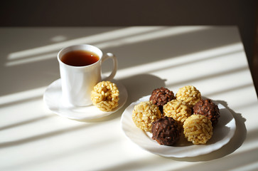sweet dessert chak chak Tatar dish round shape chocolate and yellow lie on a white plate and a white table with a Cup of tea, morning light sun beautiful light and shadow