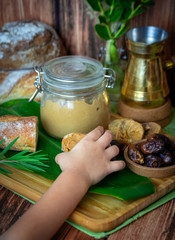 Child’s hand taking a peanut butter sandwich from the table with homemade peanut butter glass jar, fresh baguette, Turkish coffee pot, dates and figs. Close up top view shot of the breakfast table.