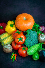 Female hand taking a pumpkin from the hip of vegetables such as pumpkin, mushrooms, zucchini, broccoli, tomato, eggplants, corn, onion, capsicum, chili, onion, parsley on the black background.