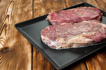 Two raw beef steaks on dark wooden table