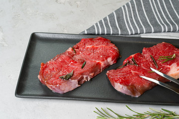 Two fresh raw meat steaks on black ceramic plate