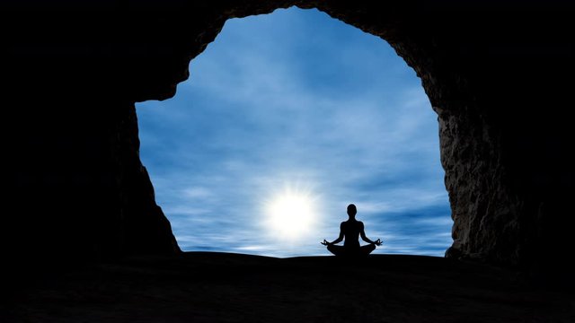 The silhouette of a female meditating at a cave entrance while watching the sun rise.