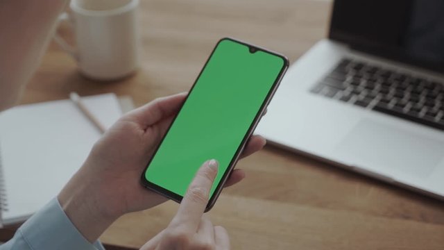 woman holding a smartphone in the hands of a green screen, chroma key, flips a finger on the screen, new technology concept