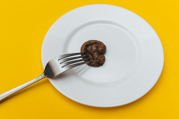 Fake news. propaganda. A fork strung artificial plastic feces which are lie on a white plate close-up. The concept of an inept cook, a crappy restaurant, bad food, a taste of shit. Bad smelling joke.