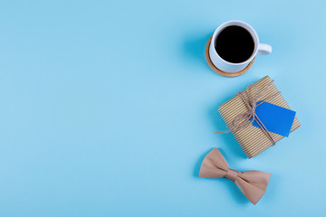 Cup of coffee, gift and bowtie on blue background. Top view in flat lay style. Happy Fathers Day Concept.