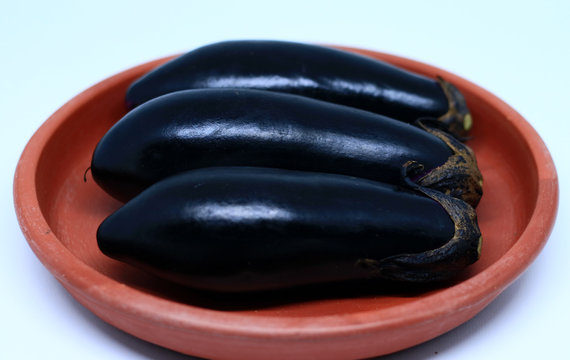 Nasubi or Japanese Eggplant on pottery plate, on white background.