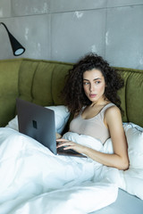 Attractive woman in white shirt using laptop and smiling at morning. Video chat and freelance working from home. concept of beautiful young woman with laptop in bed