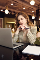 Young businesswoman in smart casual wear makes notes in a notebook in a coffee shop interior