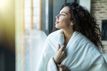 Young woman covered with blanket duver in the morning standing near window. Wake up in the cold morning