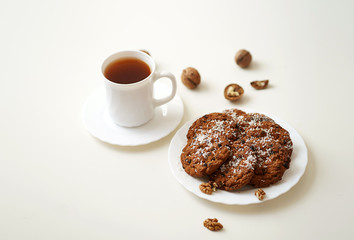 oatmeal cookies lie on a white plate sprinkled with white coconut shavings, a mug of black tea, scattered walnuts peeled and in their shells