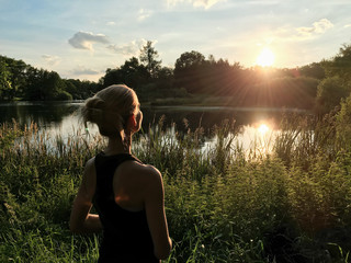 Woman enjoying peaceful moment of beautiful sunset by  lake. Self-isolation in the open air	