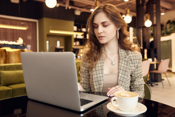 Obraz na płótnie Canvas Young businesswoman in smart casual wear drinks coffee and working on laptop