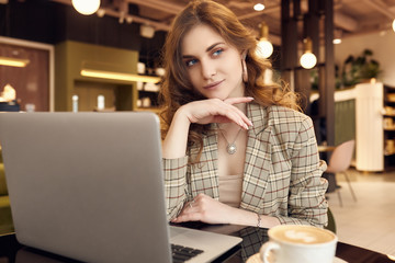 Young businesswoman in smart casual wear drinks coffee and working on laptop