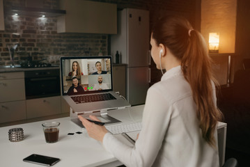 Back view of a female employee working remotely talking to her colleagues about business in a video conference on a desktop computer at home. A multiethnic business team on an online meeting.