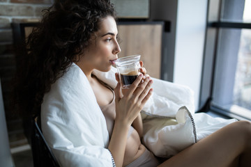 Young woman enjoying a cup of coffee sitting by a window in a sunny morning