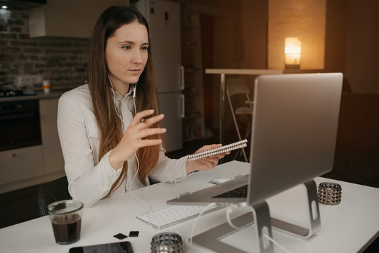 Remote work. A brunette woman with headphones working remotely online on her laptop. A girl actively discussing problems with her colleagues through a video call at her cozy home workplace.