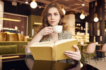 Young beautiful woman drinks coffee and reading book in cafe