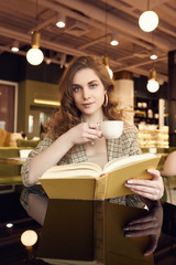 Young beautiful woman drinks coffee and reading book in cafe