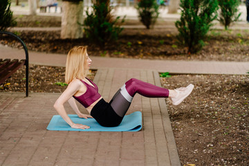 Fototapeta na wymiar girl athlete in sports apparel doing leg lifts on a Mat in Park. 