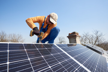 Male engineer installing stand-alone solar photovoltaic panel system using screwdriver. Electrician...